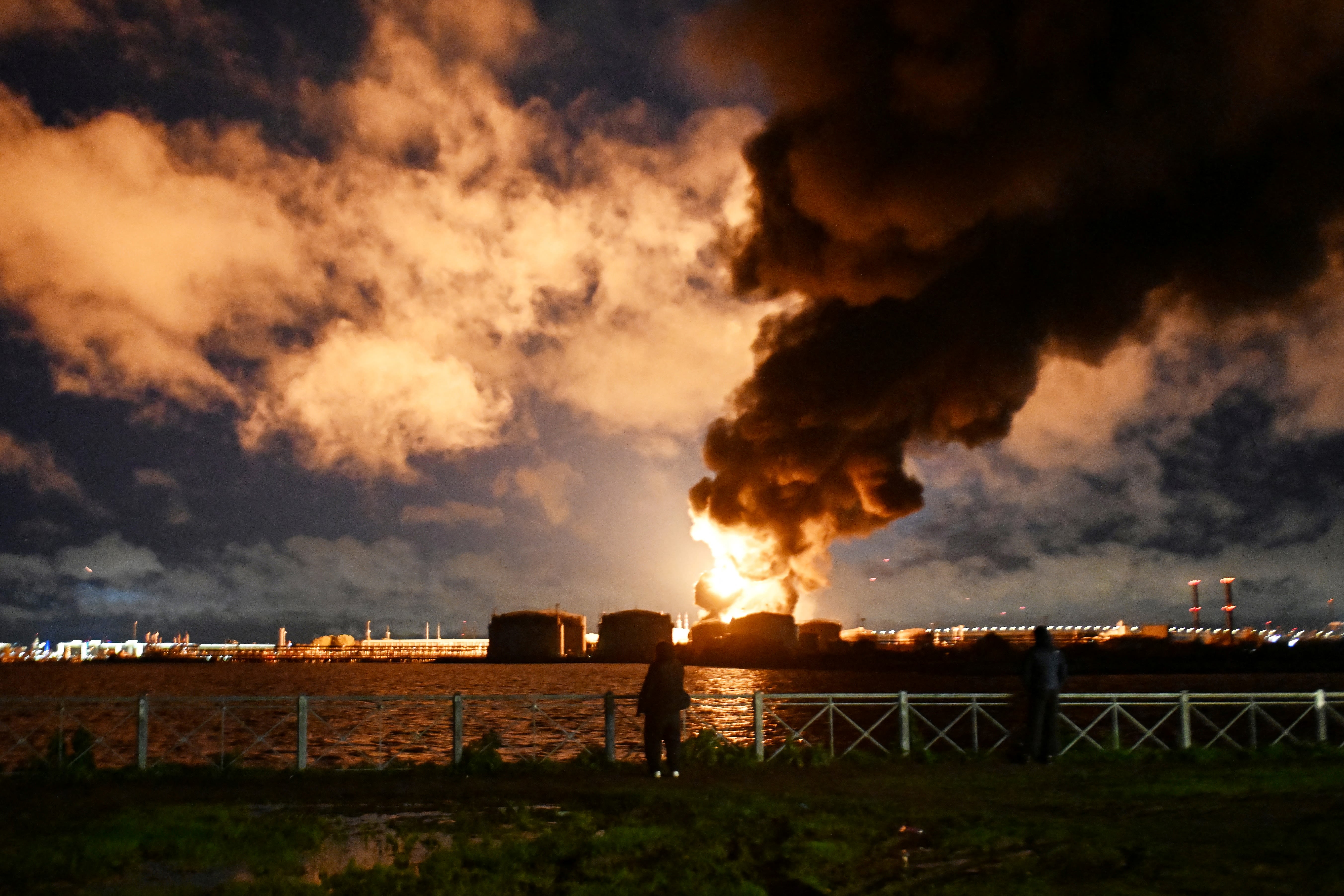 People watch the burning oil terminal following an air attack in Saint Petersburg, Russia, on October 18, 2026.