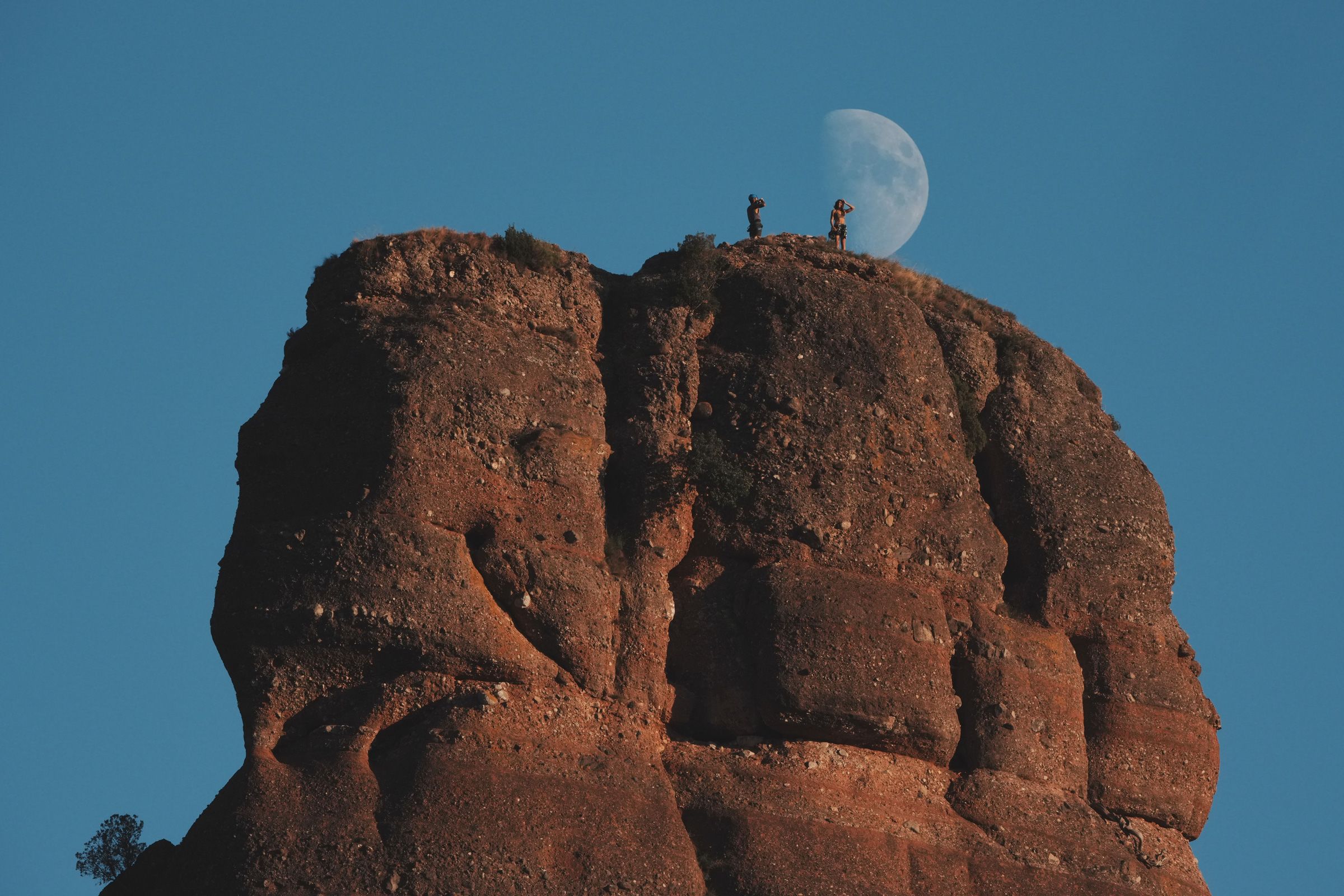 Climbers take photos while standing atop the Cavall Bernat monolith, as the moon rises behind, in the Sant Llorenc del Munt i l'Obac natural park, Matadepera, Spain, Sunday, Sept. 20, 2026.