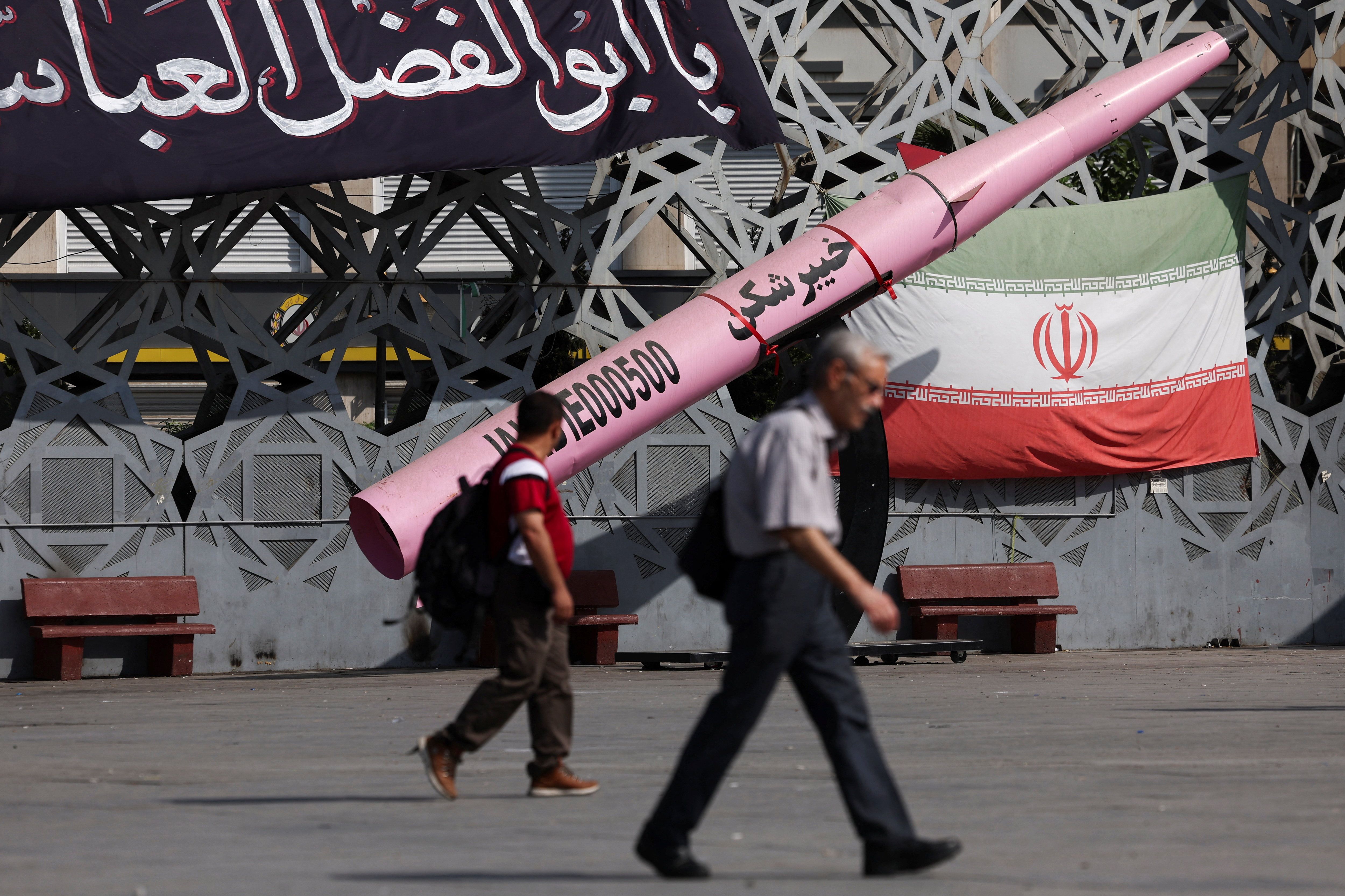 People walk next to a symbolic mockup of an Iranian missile and an Iranian flag at Imam Hussein Square in Tehran, Iran, on July 12.