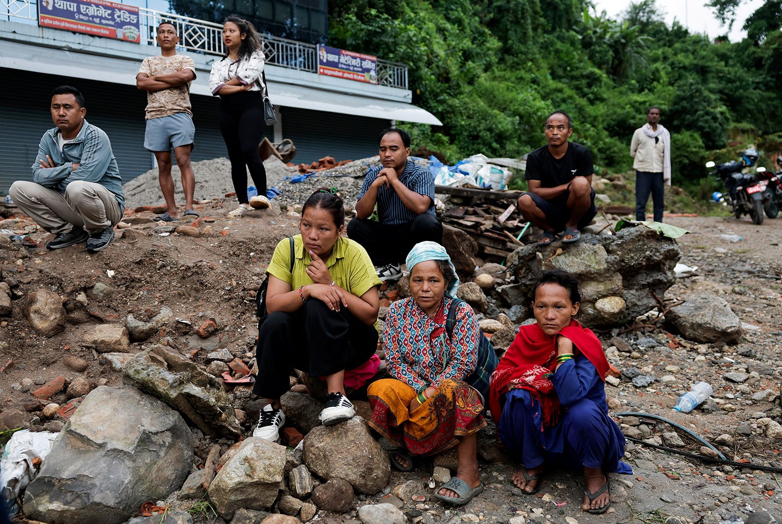 Survivors sit on debris as they wait for roads to clear to their homes following devastating floods in Trishuli, Nuwakot district, Nepal, August 27, 2026.