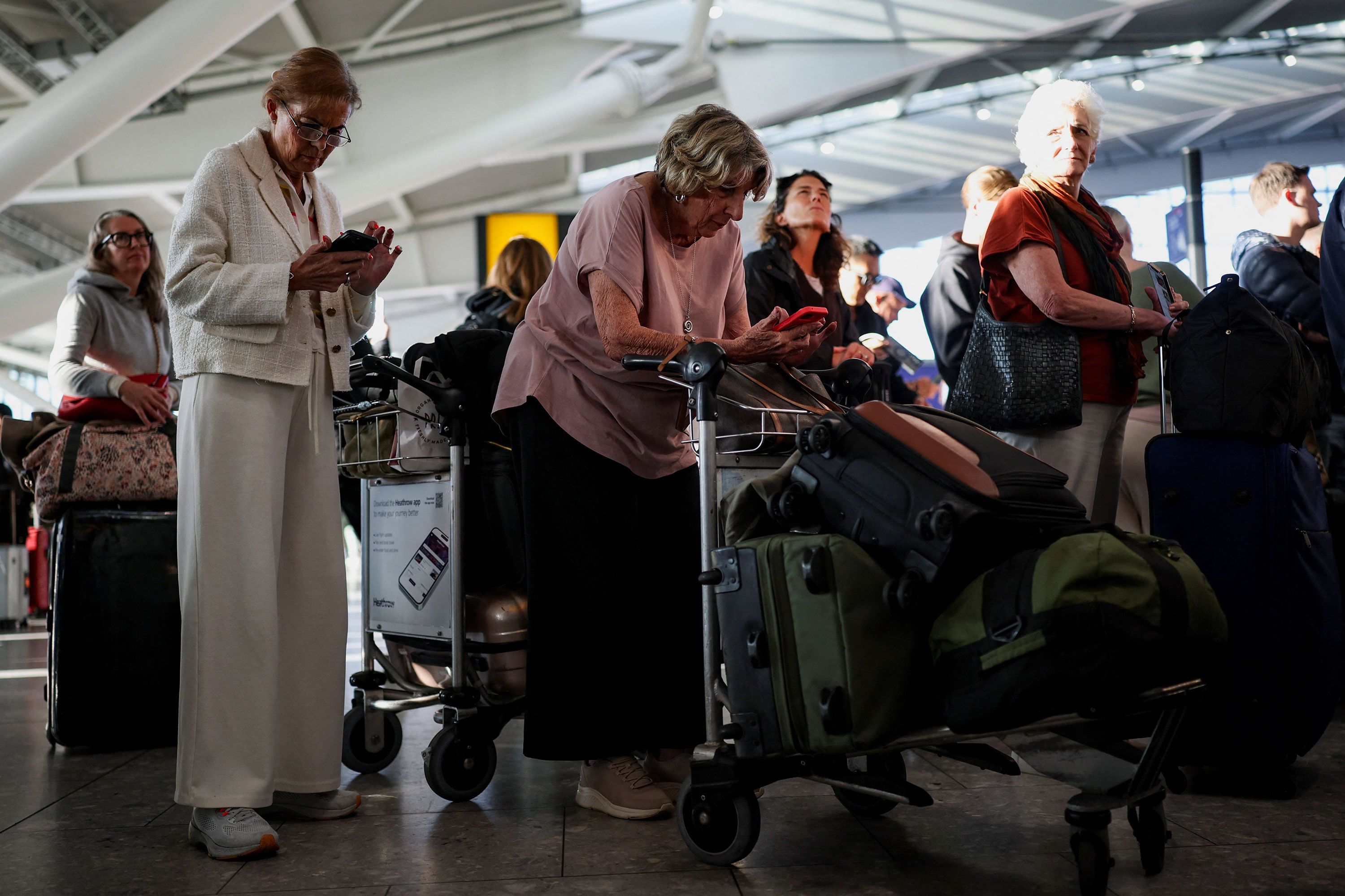 Stranded passengers use their phones after some departing flights were cancelled, at Heathrow Airport's Terminal 5 in London, on Tuesday, September 8.
