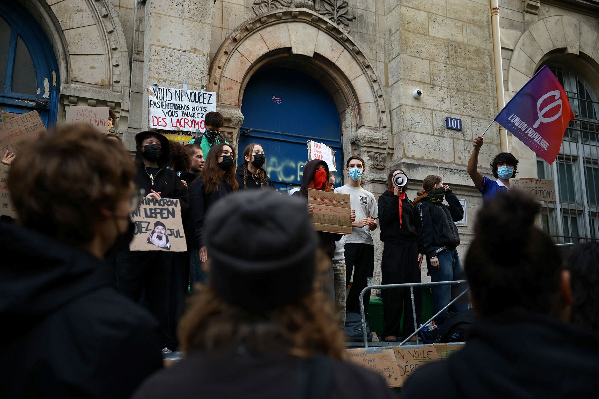 A student holds a flag of La France Insoumise (France Unbowed - LFI) party as French high school students gather outside the Lycee Voltaire high school as part of nationwide protests to demand the hiring of substitute teachers, increased resources and better learning conditions, in Paris, as more than 400 schools remain closed following days of student protests that have escalated into violence in some places, France, October 2, 2026.  REUTERS/Sarah Meyssonnier