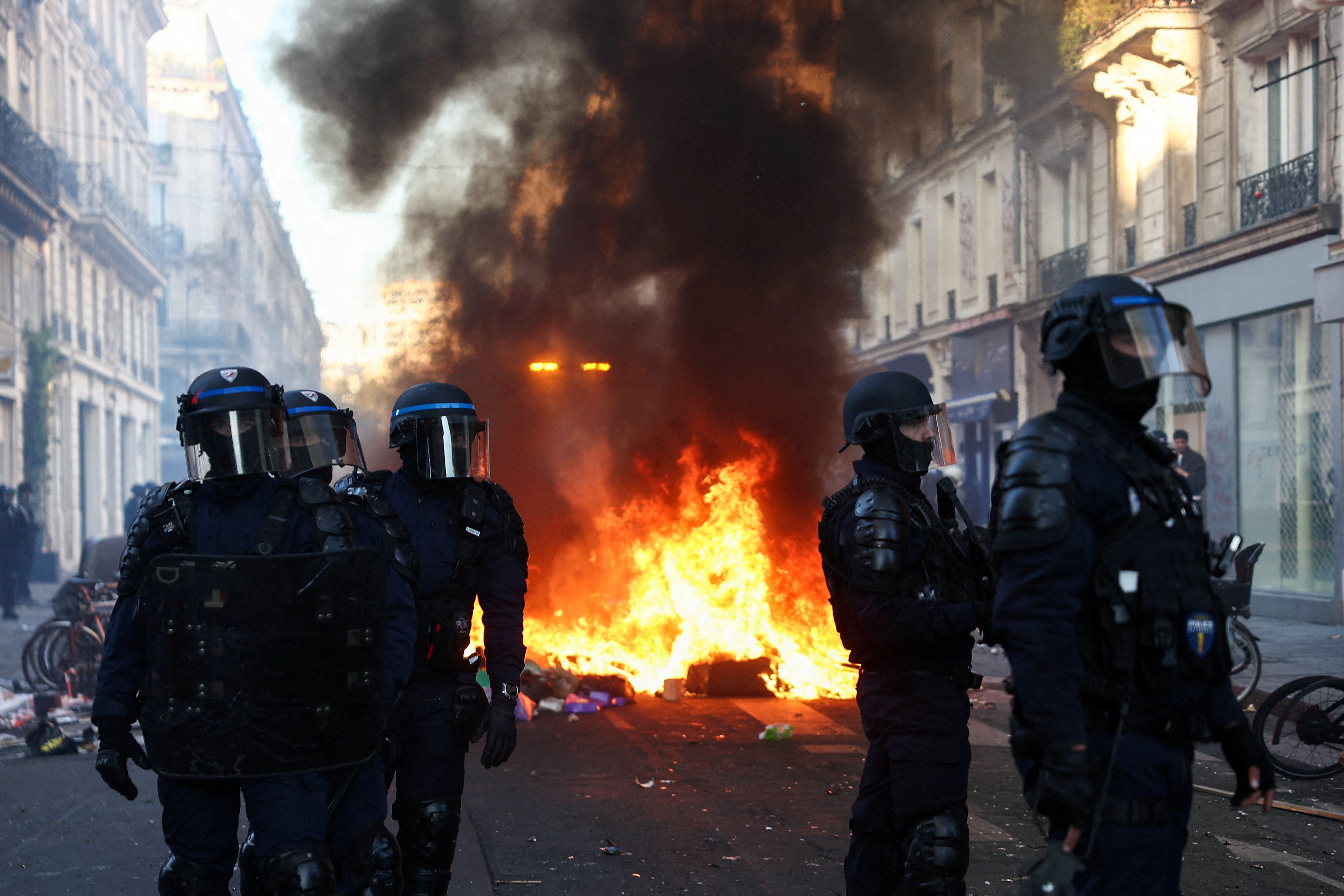 A fire burns as Police officers in riot gear stand guard, during civil unrest, the day after a national day of demonstrations against the cost of living and rising fuel prices, in Paris, France, October 18, 2026.