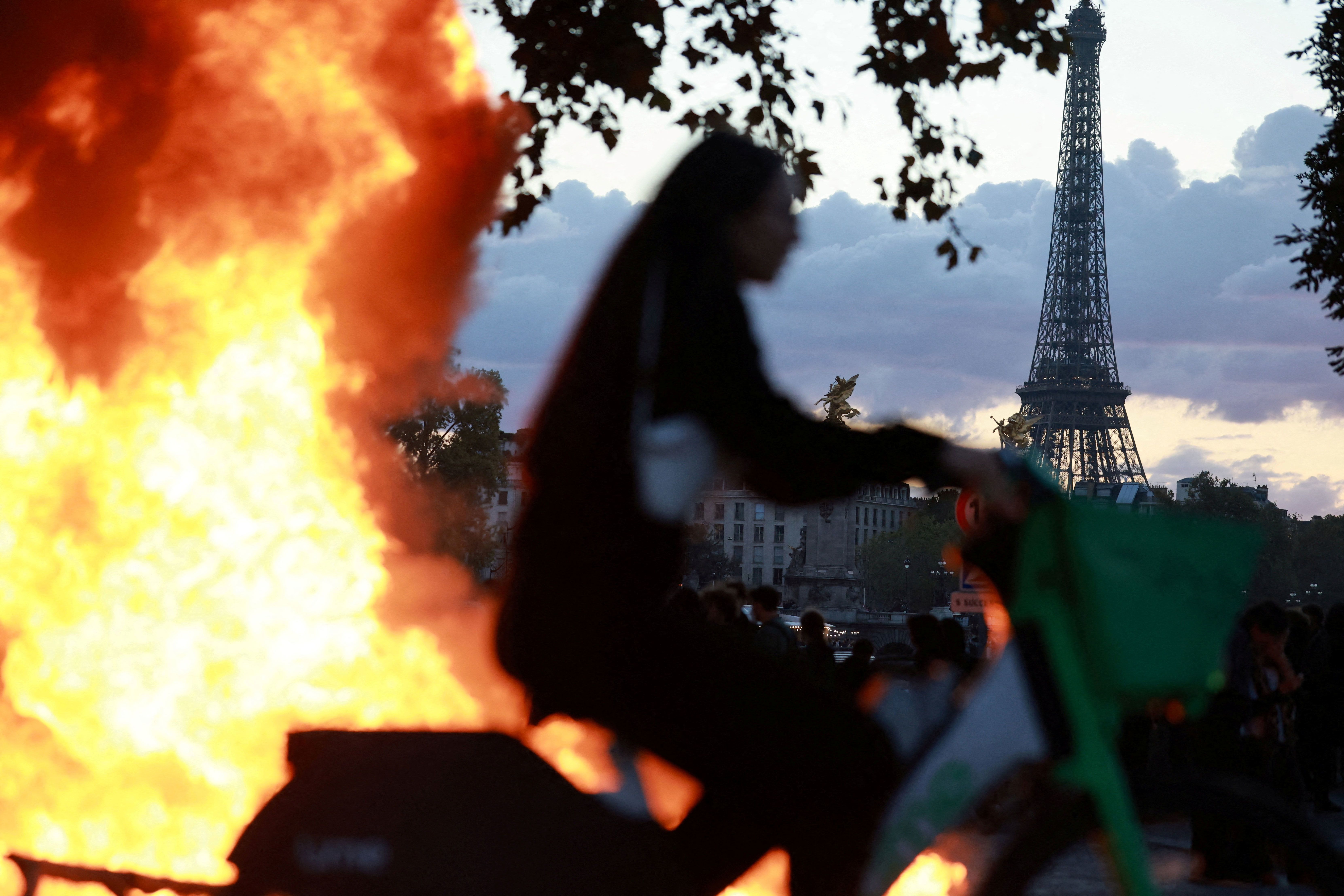 A woman rides a bicycle past a burning barricade near the Tuileries Garden with the Eiffel Tower in the background, amid clashes during a day of demonstrations against the cost of living and rising fuel prices in Paris as part of nationwide protests.