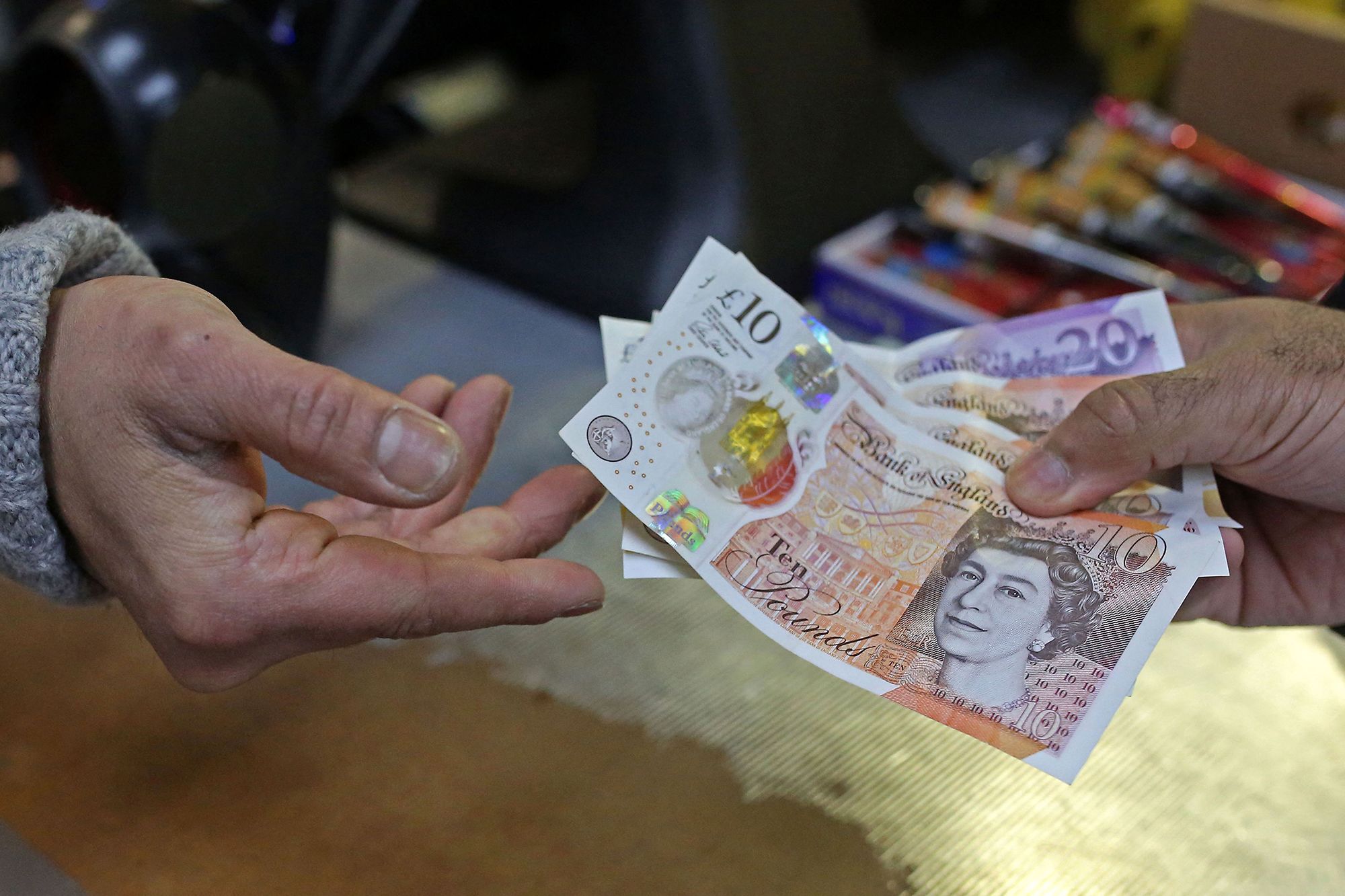 A shopkeeper (L) passes a customer their change in GBP pound sterling ten and twenty pound notes, at a shop in east London on March 31, 2023. 
